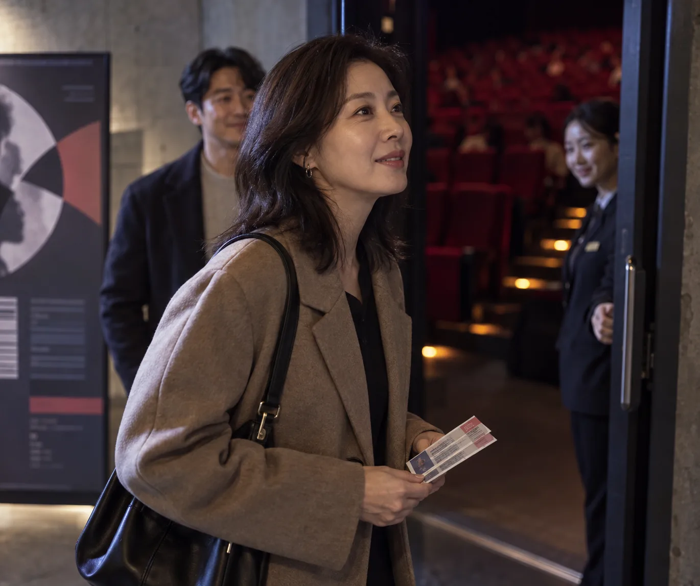 영화관 입구에서 표를 든 채 미소 짓는 여성과 뒤따르는 남성