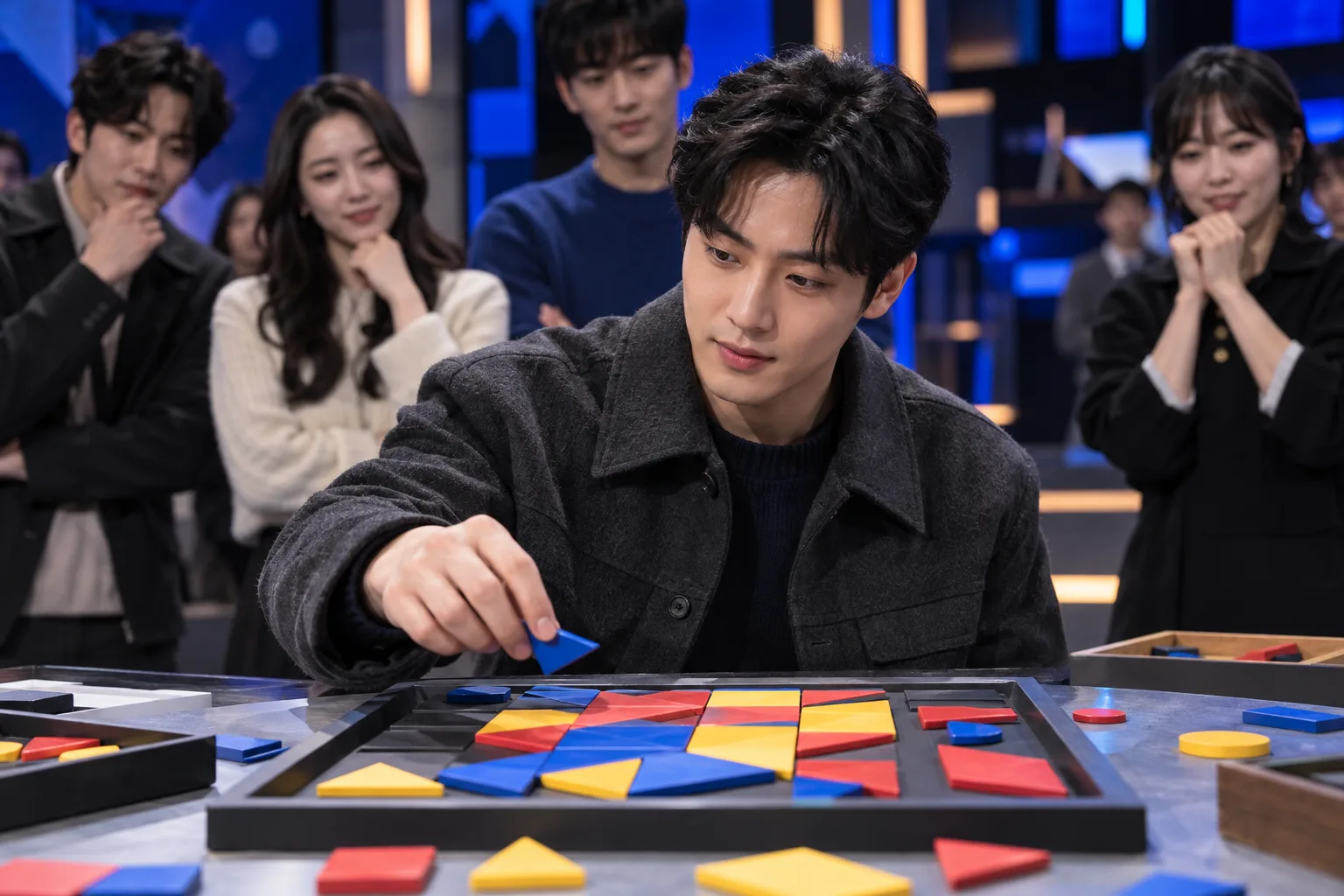 한 참가자가 색색의 타일 퍼즐에 조각을 놓고, 뒤에서 다른 참가자들이 지켜본다.