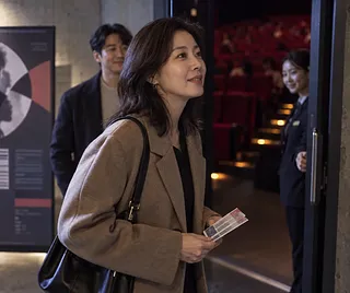 Mujer sonriente con entradas en la puerta de un cine y un hombre detrás