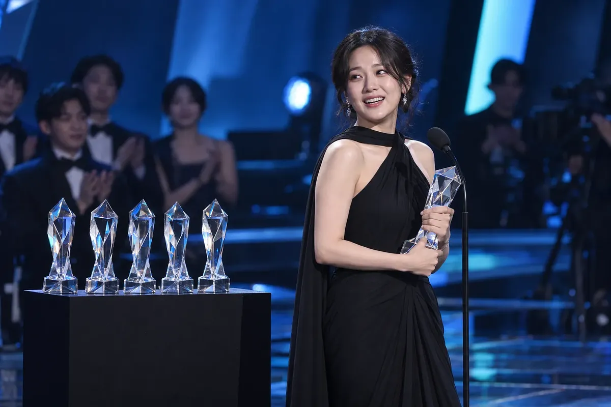 검은 드레스를 입은 여성이 무대에서 크리스털 트로피를 들고 미소 짓는 모습