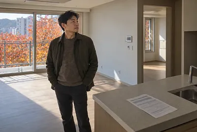 A man looks around a vacant apartment, with a loan notice on the kitchen counter.